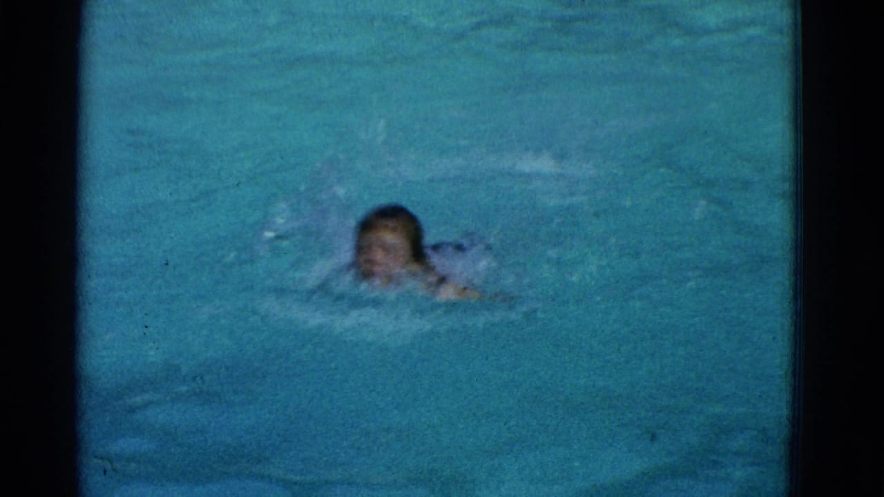A swimmer faces the camera while moving through blue pool water in supported 1953 Yonkers 8mm home-movie footage.