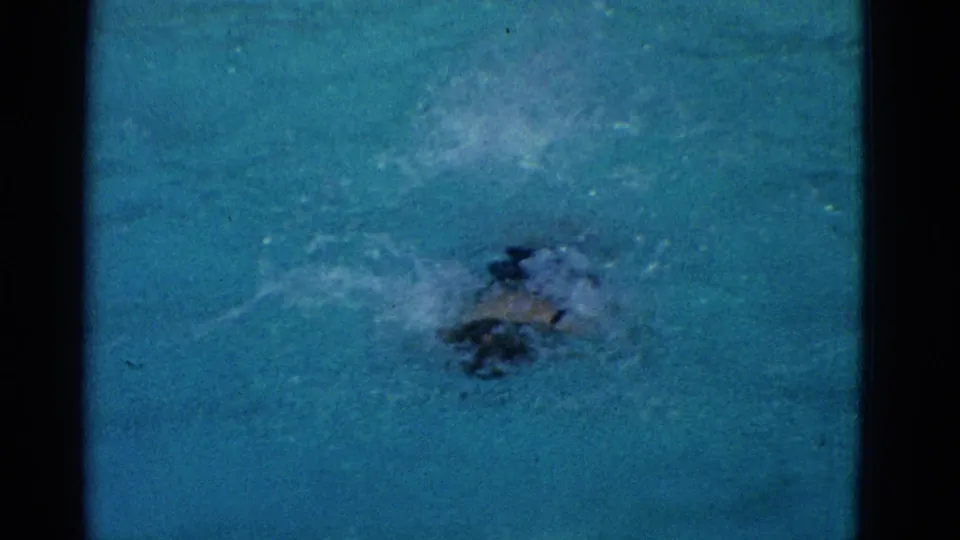 The swimmer is mostly submerged as splashes break across the blue pool surface in the 1953 Yonkers 8mm home-movie scene.