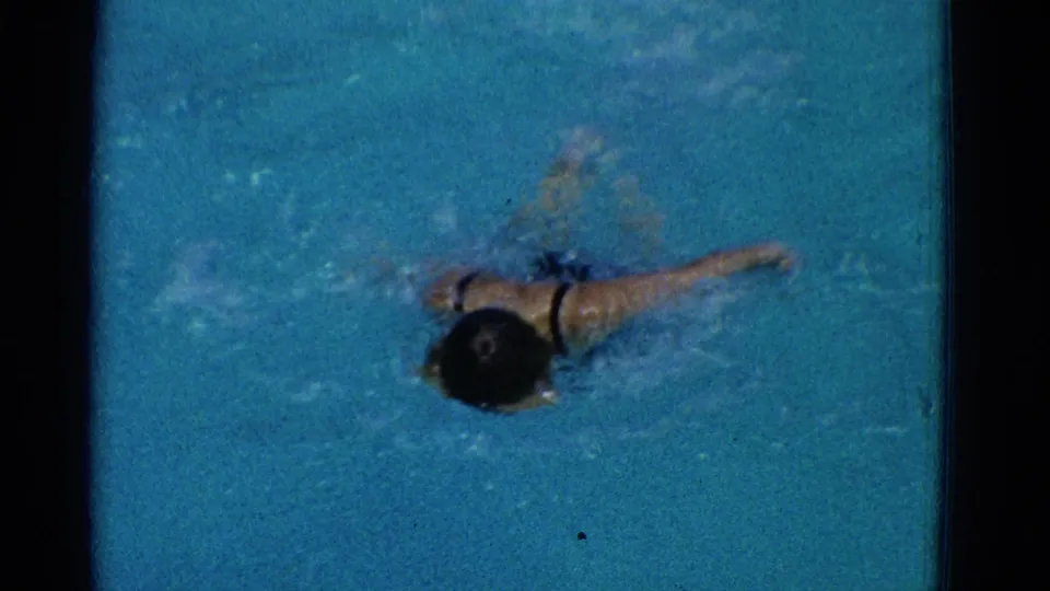 1953 Yonkers 8mm frame showing a young swimmer moving through blue pool water with one arm extended and bubbles around the body.