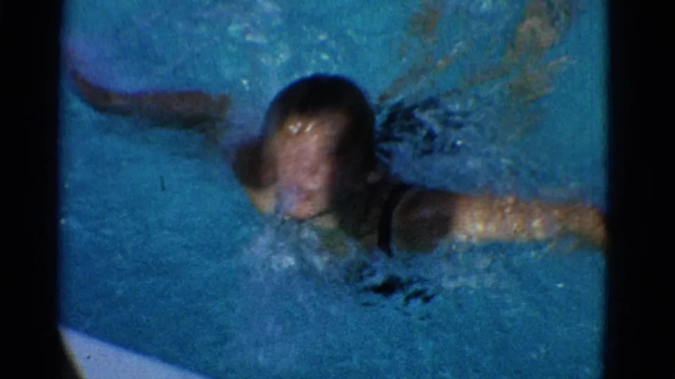 1953 Yonkers 8mm frame showing the young swimmer closer to camera, face blurred by motion and water while arms move through the pool.
