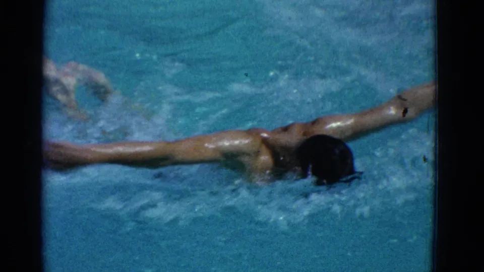 1953 Yonkers 8mm frame showing the swimmer face-down with arms spread wide across blue water during a butterfly-style movement.