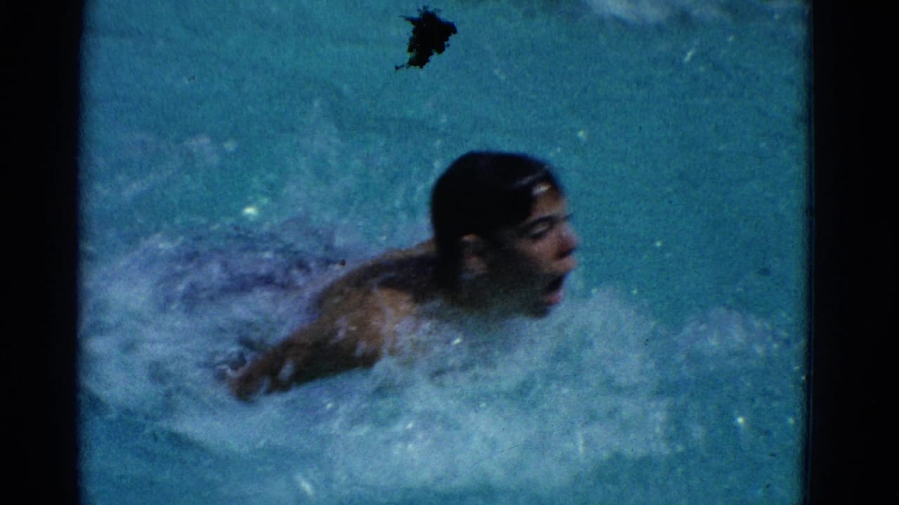 Man in a pool raises his head while swimming through splashing blue water.