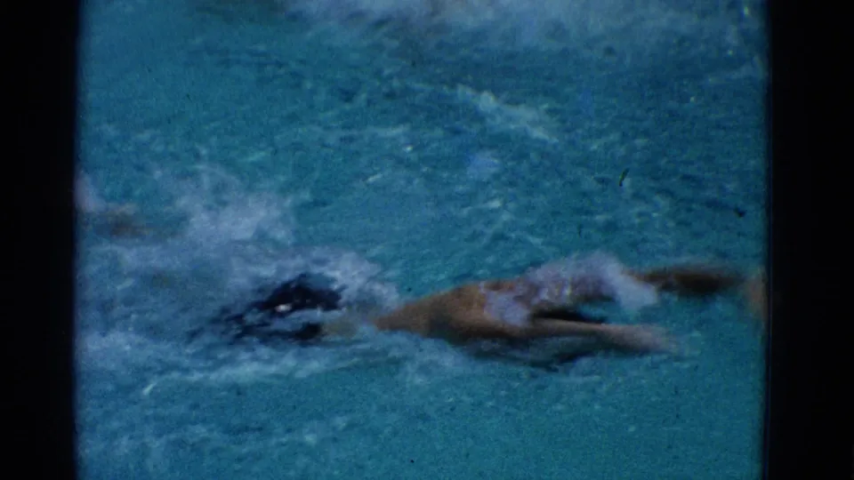 The swimmer continues across the pool in a 1953 Yonkers 8mm frame, his body stretched through the water with visible splashing.