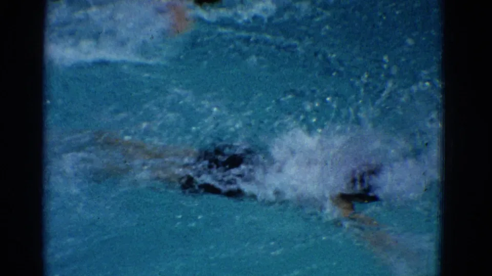 A 1953 Yonkers pool frame shows the swimmer low in the water, partly hidden by spray and blur from the stroke.