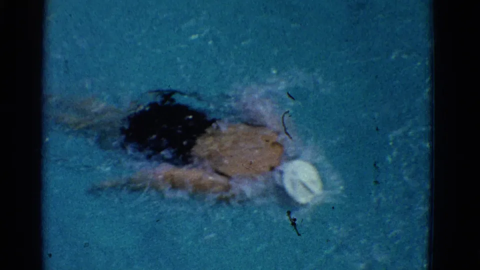 The swimmer appears from above in the pool, wearing a white cap as he moves through blue-green water in the 1953 Yonkers footage.