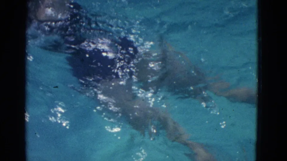 The swimmer appears partly submerged amid bubbles and reflections, with legs visible under the blue water near the end of the clip.
