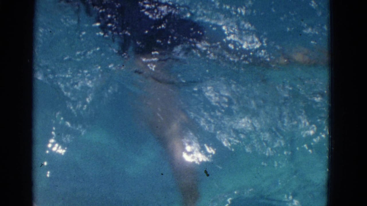 Swimmer partly visible under blue pool water with bright reflections and dark film borders.