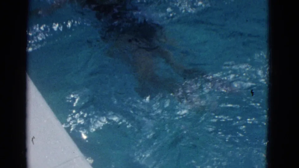 1953 Yonkers pool frame with rippling blue water, glare on the surface, and a pale pool edge visible along one side.