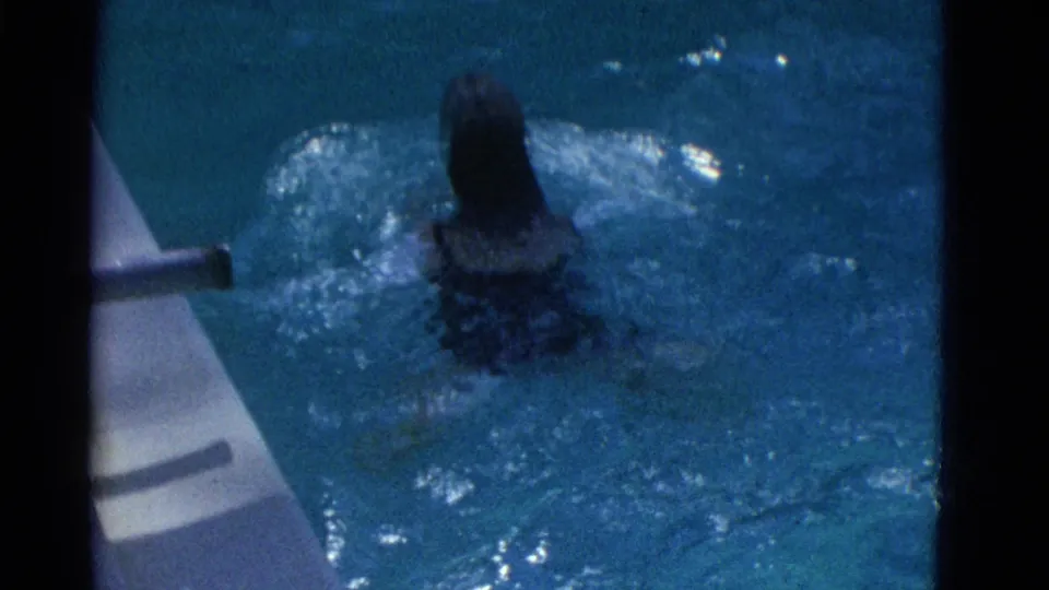 1953 Yonkers home-movie frame showing a swimmer moving near the pool edge, with splashes, railings, and heavy 8mm frame borders.
