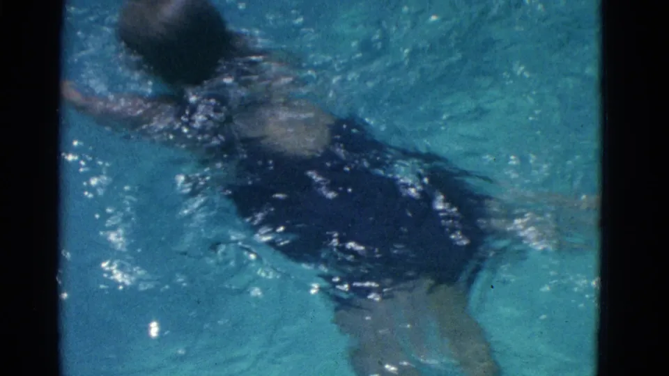 A swimmer in a purple bathing suit moves through blue pool water in 1953 Yonkers home-movie footage.