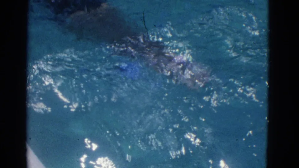 The swimmer is mostly submerged amid ripples and splashes in the blue pool water.