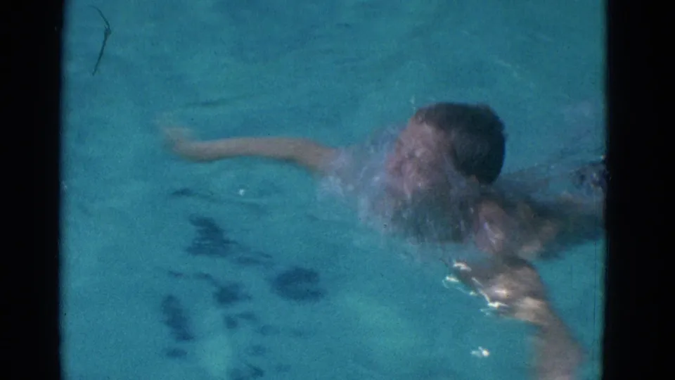 1953 Yonkers 8mm frame of a young swimmer surfacing with arms spread during a stroke in bright pool water.