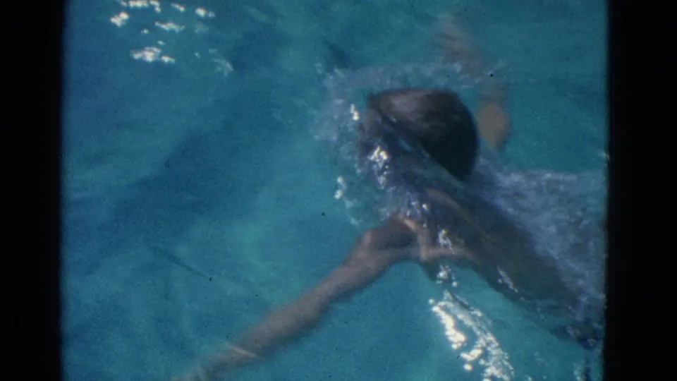 1953 Yonkers 8mm frame of a swimmer partly submerged, with an arm extended and splashes across the pool surface.