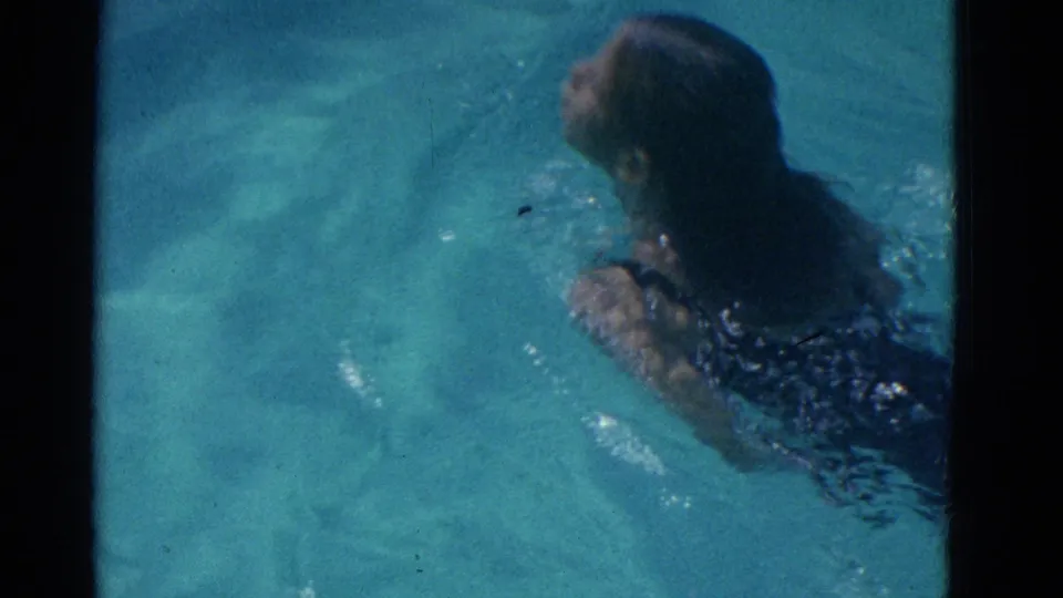 A likely young swimmer surfaces during breaststroke in a sunlit pool, supported by the Yonkers 1953 clip metadata.