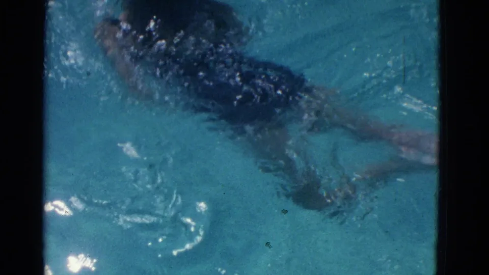 Overhead 8mm view of a likely young swimmer continuing breaststroke through turquoise pool water in Yonkers footage.