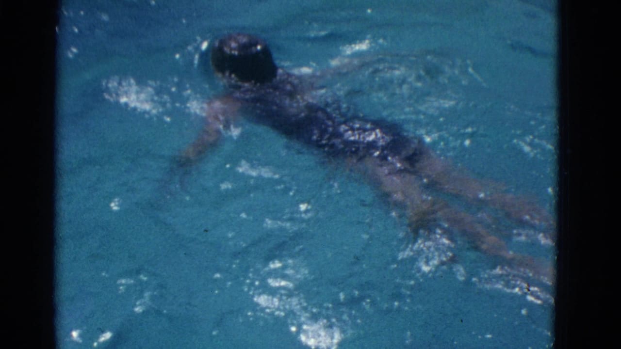 In 1953 Yonkers home-movie footage, a girl in a dark swimsuit swims near the surface of clear blue pool water.