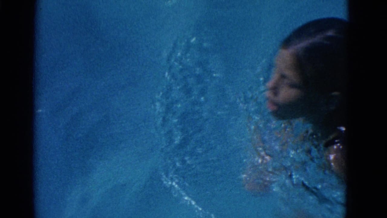 In 1953 Yonkers home-movie footage, a swimmer moves through blue pool water with face, hair, shoulders, and splashes visible.
