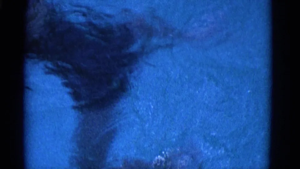 A submerged figure moves below the blue pool surface in the 1953 Yonkers home movie, softened by water, grain, and motion blur.