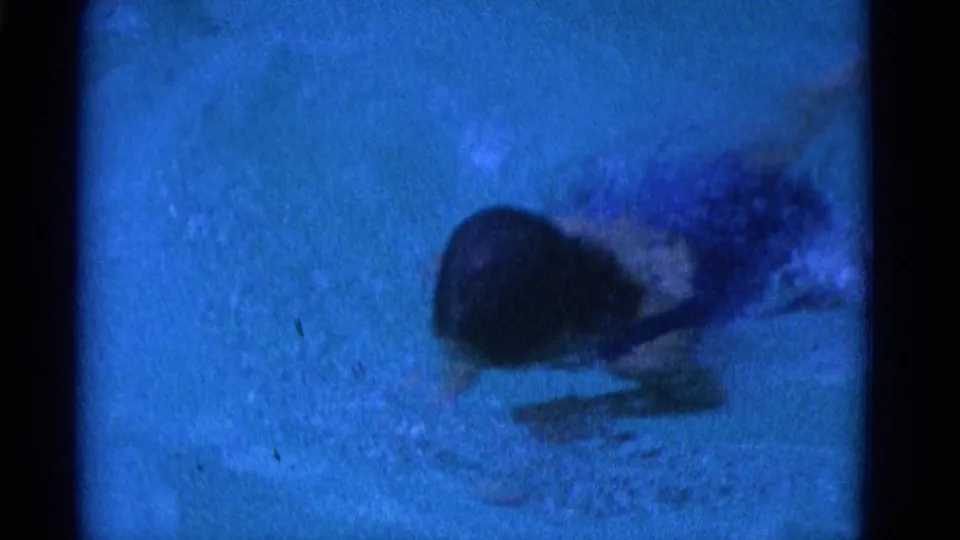 1953 Yonkers 8mm frame of a swimmer partly submerged in blue pool water, with motion blur, bubbles, and dark frame edges.