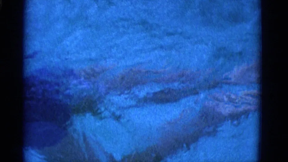 Blue-tinted 1953 8mm frame from Yonkers showing rippling water and heavy grain before the swimmer is clearly visible.