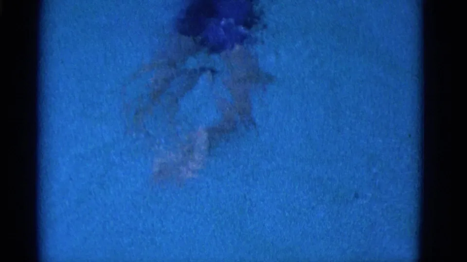 Overhead 1953 Yonkers home-movie frame of a swimmer partly underwater, with arms extended and hair floating in a blue pool.