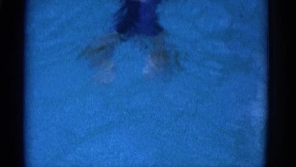 Blue-tinted 8mm pool frame showing the swimmer distorted by water movement and film blur in the Yonkers home movie.
