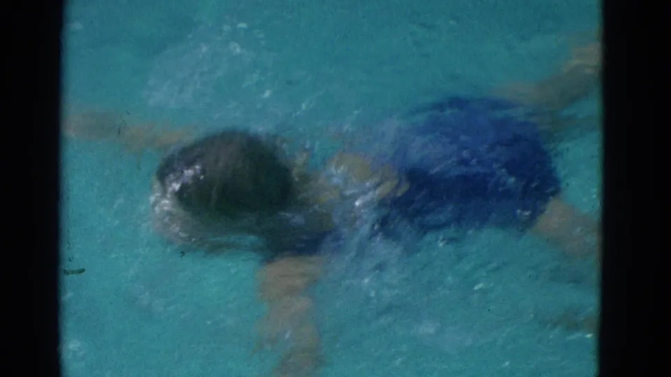 The child is partly submerged while swimming through blue water, with motion blur and splashes visible in the 8mm frame.