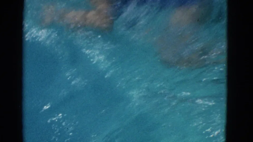 A blurred underwater view shows the child swimmer moving through turquoise water, with the body softened by refraction and film grain.