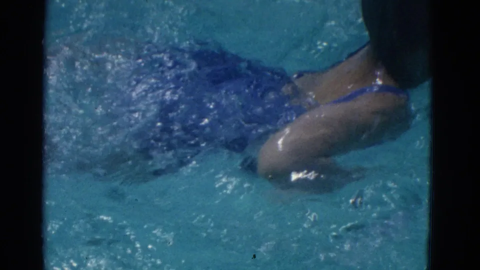 1953 Yonkers home-movie frame with a swimmer in a dark blue swimsuit moving through sunlit pool water.