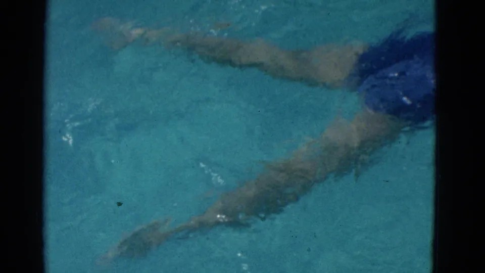 1953 Yonkers home-movie frame showing the swimmer mostly underwater, with limbs blurred by turquoise pool water.