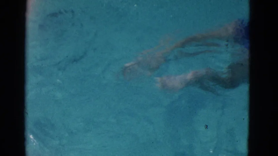 1953 Yonkers home-movie frame with the swimmer partly visible underwater near the right edge of the pool view.