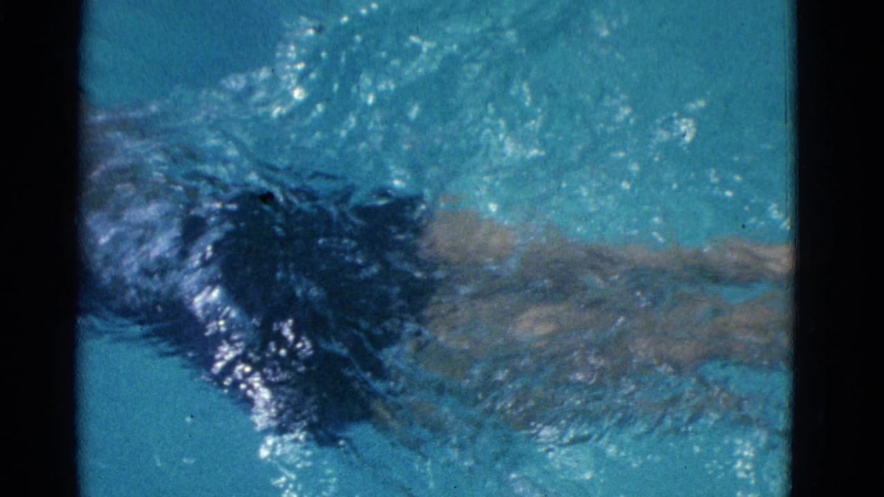 Swimmer mostly submerged in blue water, with dark hair and legs visible amid surface ripples.