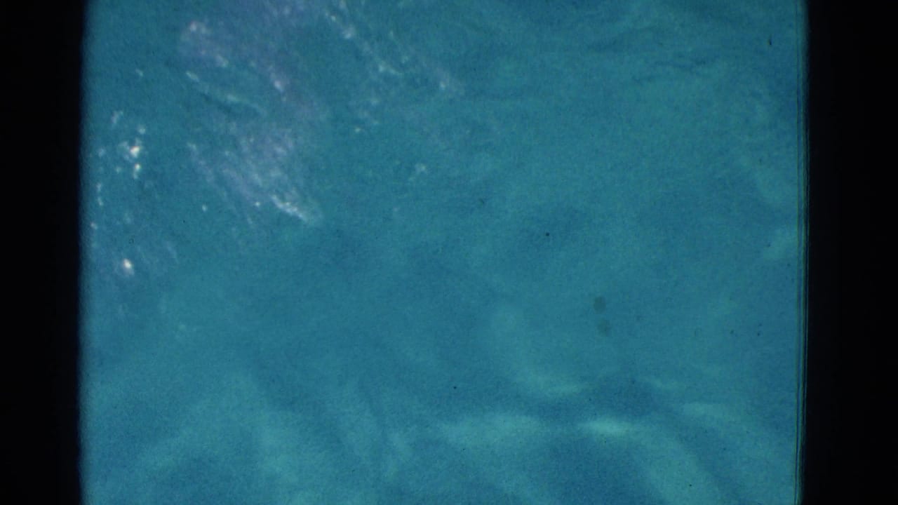 1953 Yonkers home-movie frame showing a swimmer partly obscured under turquoise water with film grain and dark frame edges.