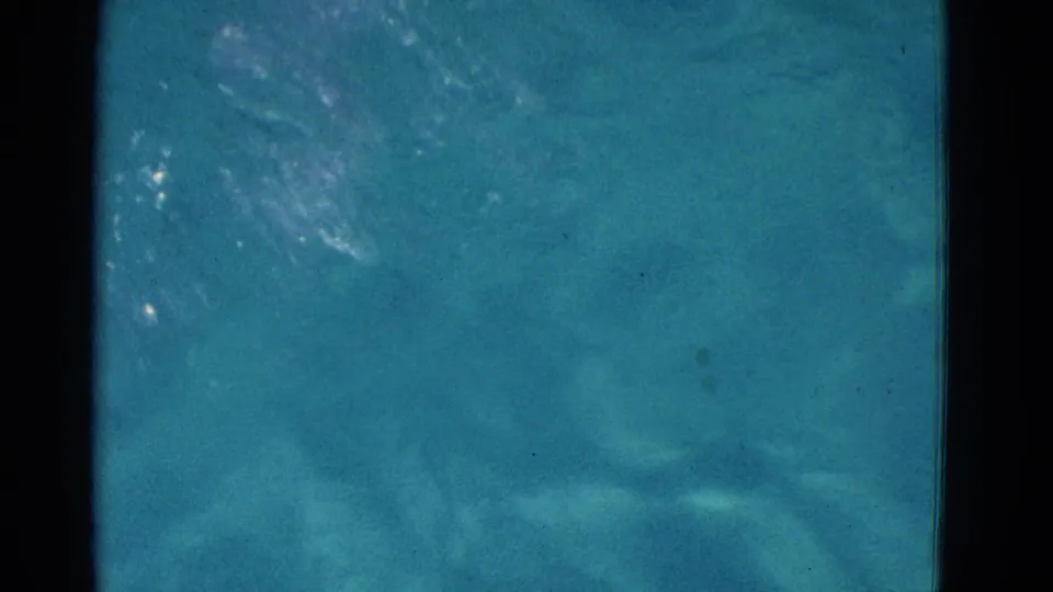 1953 Yonkers home-movie frame showing a swimmer partly obscured under turquoise water with film grain and dark frame edges.