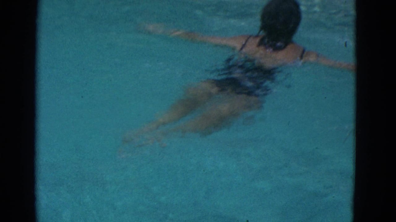 Swimmer in a dark swimsuit moves through turquoise pool water with arms extended.