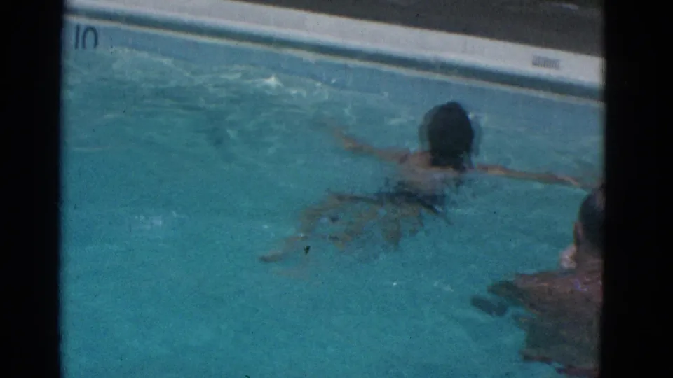 1953 Yonkers pool frame with a swimmer near white coping and a partially visible poolside person at the right edge.