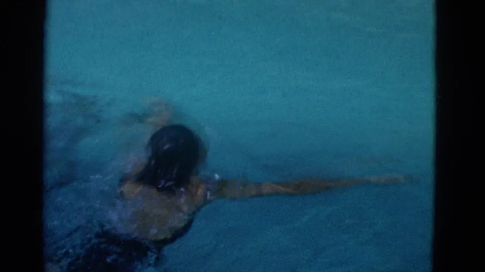 1953 Yonkers 8mm frame showing a swimmer partly submerged in blue-green pool water, arm extended through ripples.