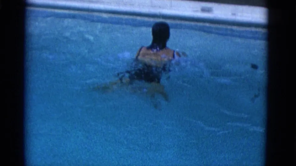 The swimmer is viewed from behind in blue water, with the pool edge visible near the top of the 8mm frame.