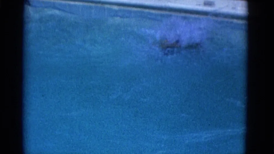 A soft, grainy 8mm frame shows the swimmer partly obscured by water and motion during the lap.