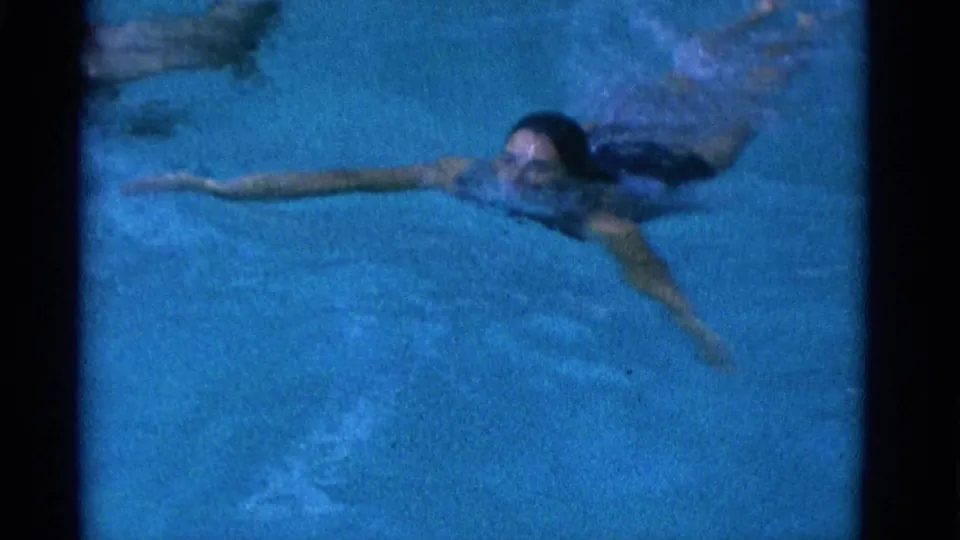 A woman in a dark swimsuit swims freestyle across a blue pool in 1953 Yonkers home-movie footage.
