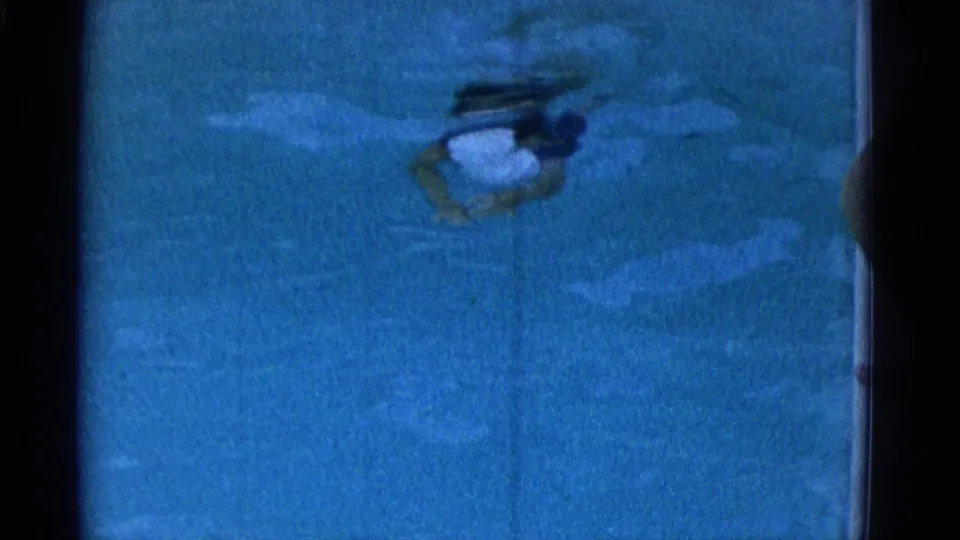 A swimmer moves near the surface of a blue pool in the 1953 Yonkers 8mm footage, seen through soft focus and visible film grain.
