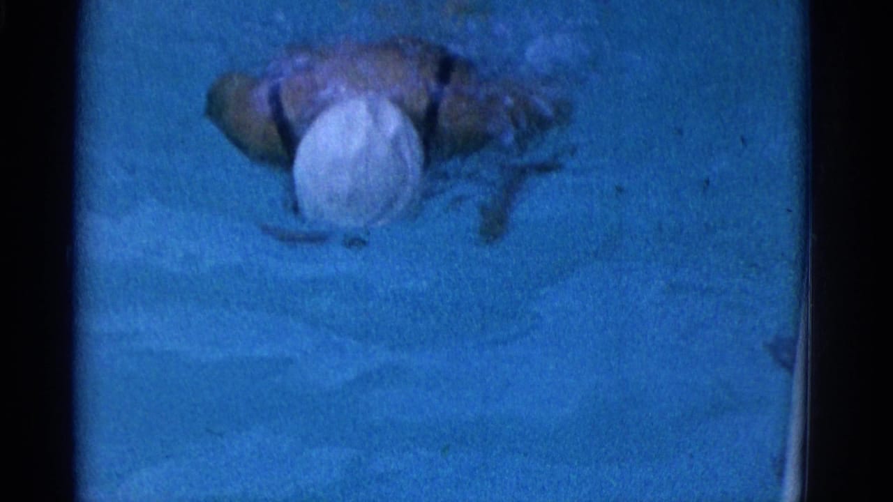 Underwater swimmer in a white cap and dark bathing suit moving through blue pool water.