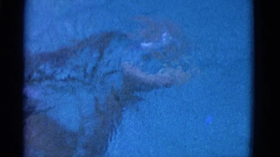 Underwater 1953 Yonkers frame showing the swimmer in a dark suit finishing a stroke, with an extended leg and soft blue film color.