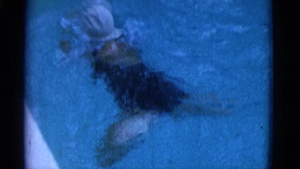 1953 Yonkers home-movie still showing a woman in a white swim cap and dark swimsuit swimming close to a pale pool edge.