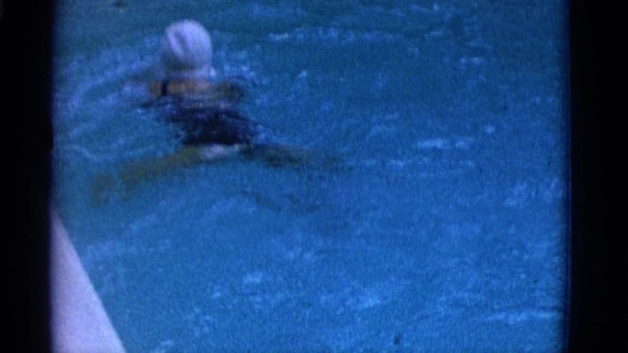 1953 Yonkers home-movie frame showing a swimmer in a white cap crossing blue pool water with ripples and dark film borders.