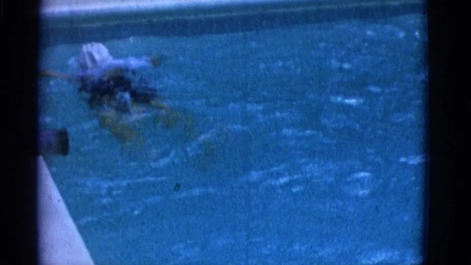 1953 Yonkers 8mm frame with the swimmer partly submerged and blurred by motion in blue pool water.