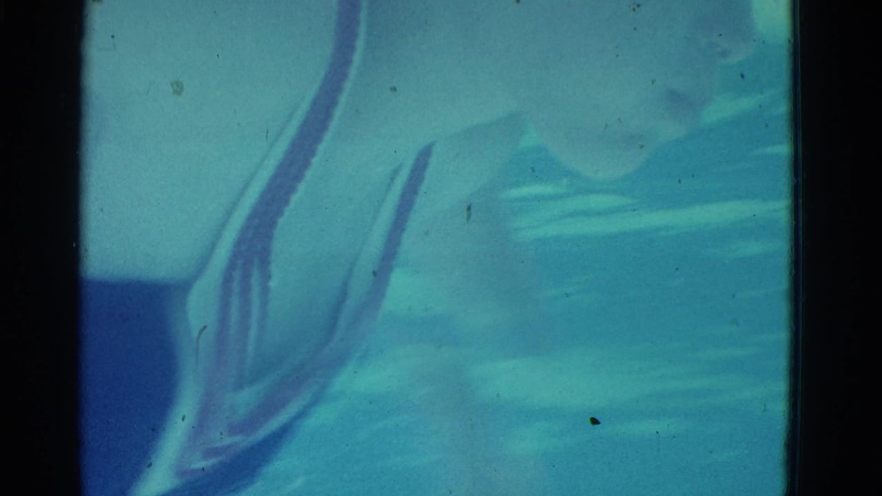Underwater blue-green frame with a swimmer form near the left side and visible film gate edges.