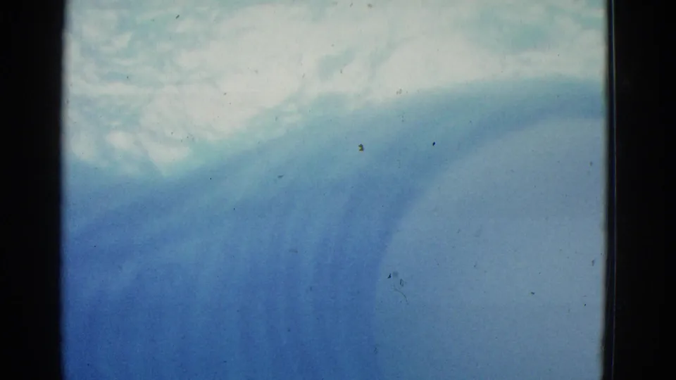 1953 color 8mm underwater frame with a faint swimmer form, pale blue water, and wavering surface light.
