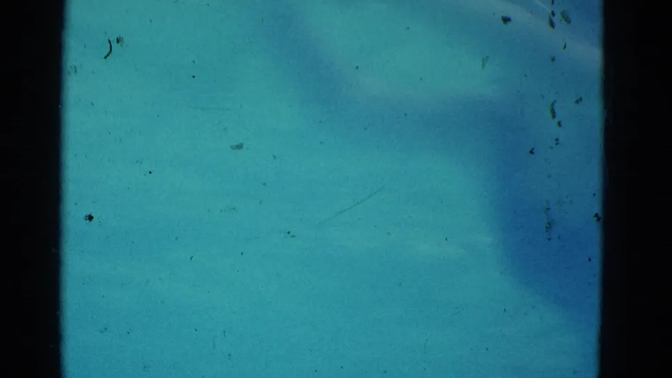 Final underwater frame from the Yonkers home movie, showing blurred swimmer movement in turquoise water with 8mm specks and edge darkening.