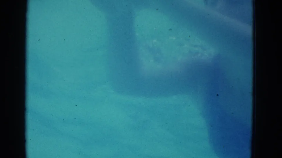 1953 Yonkers 8mm frame with a swimmer partly visible below blue pool water, softened by color shift, grain, and exposure variation.